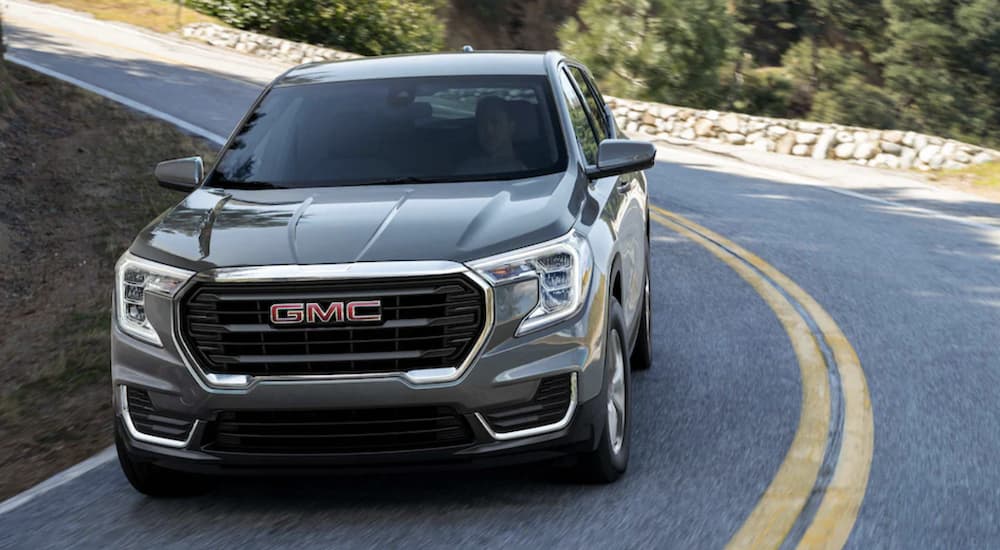 A grey 2023 GMC Terrain for sale is shown driving.