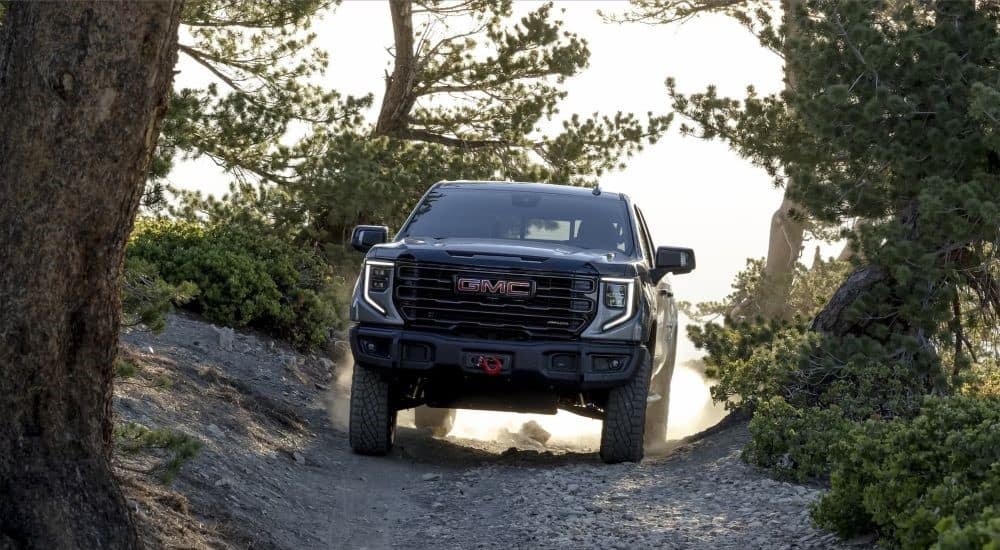 A grey 2024 GMC Sierra 1500 AT4X AEV is shown driving on a dusty trail after leaving a GMC dealer.