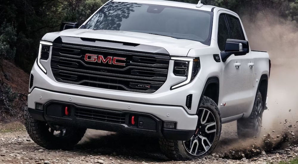 The smallest GMC Sierra for sale, a white 2024 GMC Sierra 1500 AT4, is shown driving off-road.