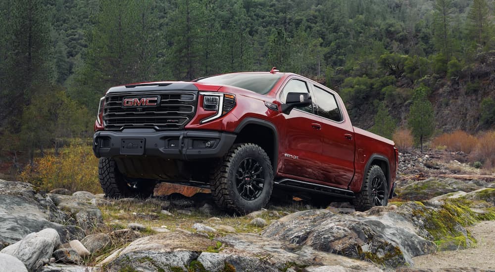 A red 2024 GMC Sierra 1500 AT4X is shown driving up a rocky cliff after visiting a dealership with a GMC Sierra 1500 for sale.