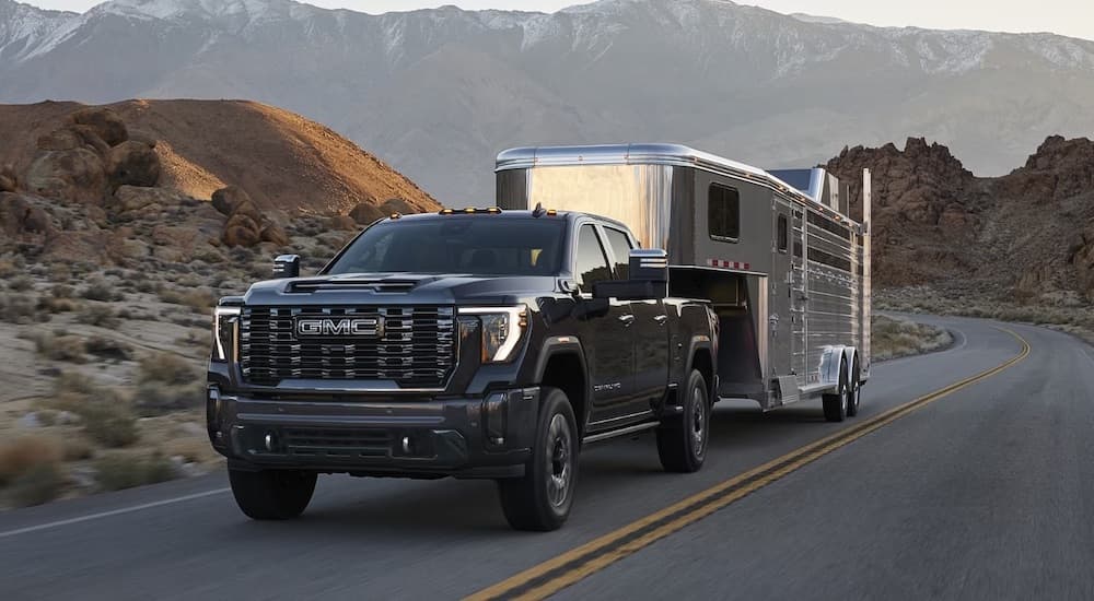 A black 2024 GMC Sierra 2500 HD is shown towing a camper van.