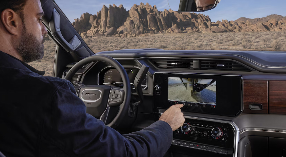 A driver using the rear camera screen in a 2024 GMC Sierra 3500 HD Denali for sale.