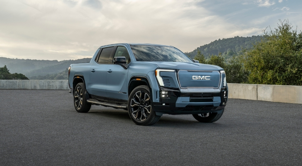 A blue 2025 GMC Sierra EV Denali parked near a wall.