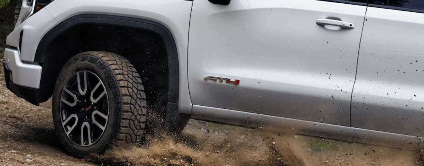 A close-up on the front wheels of a white 2023 GMC Sierra 2500 HD AT4 are shown while driving off-road.
