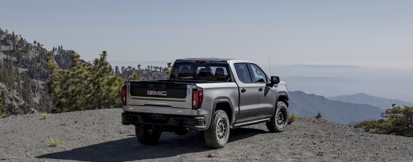 A grey 2024 GMC Sierra AT4x AEV is shown from the rear at an angle while off-road.