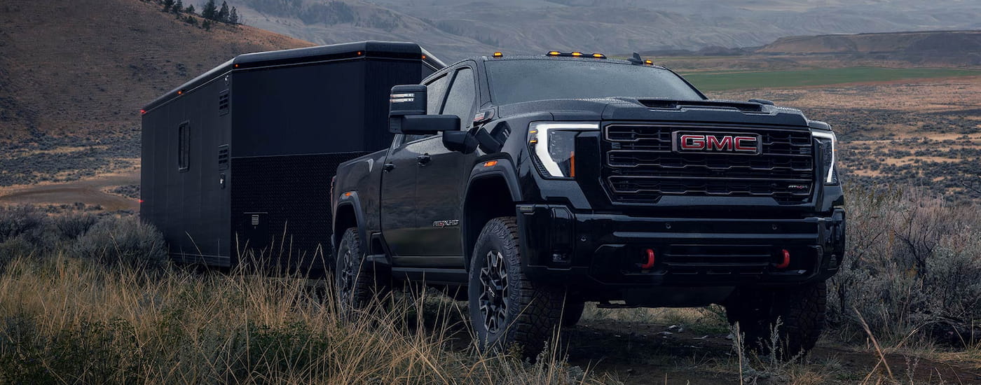 Black 2026 GMC Sierra 2500 HD towing a trailer driving down a road.