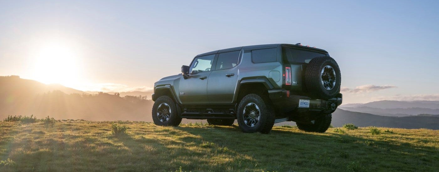 Rear view of a green 2024 GMC Hummer EV parked on a grassy hill.