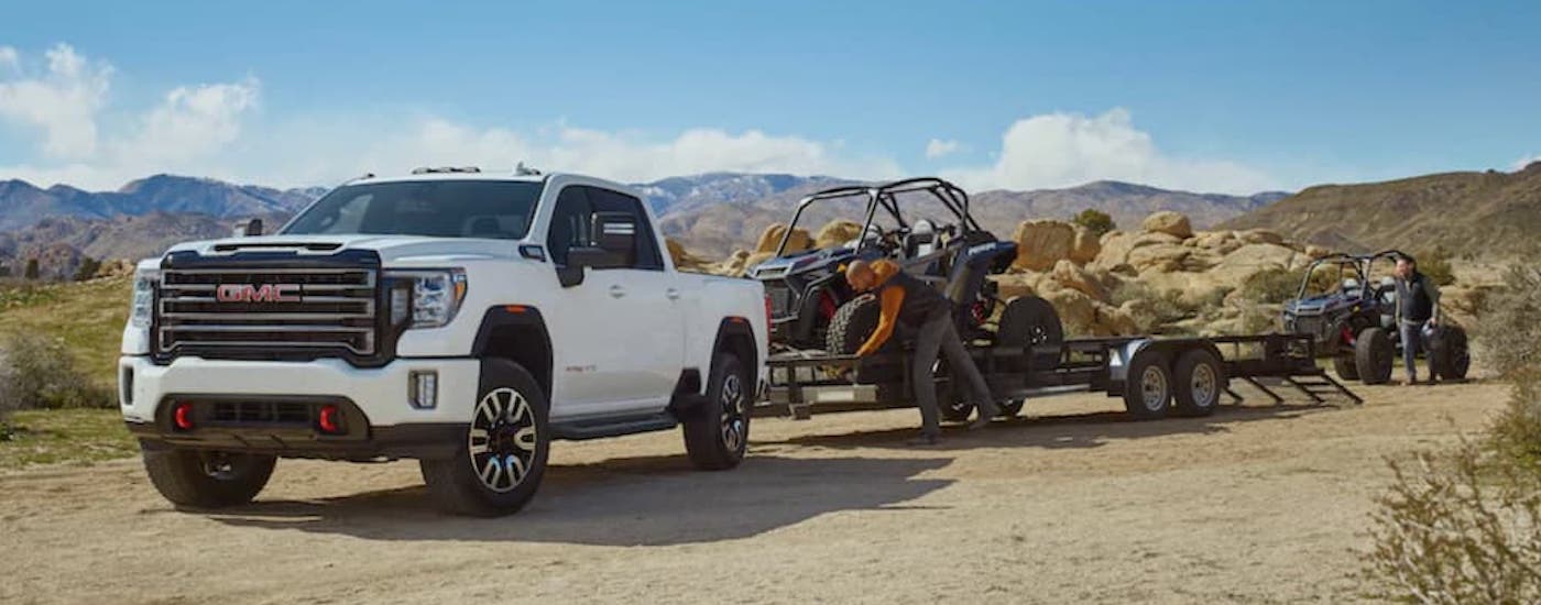 A white 2021 GMC Sierra 2500 HD AT4 is shown from the front while unloading UTVs.