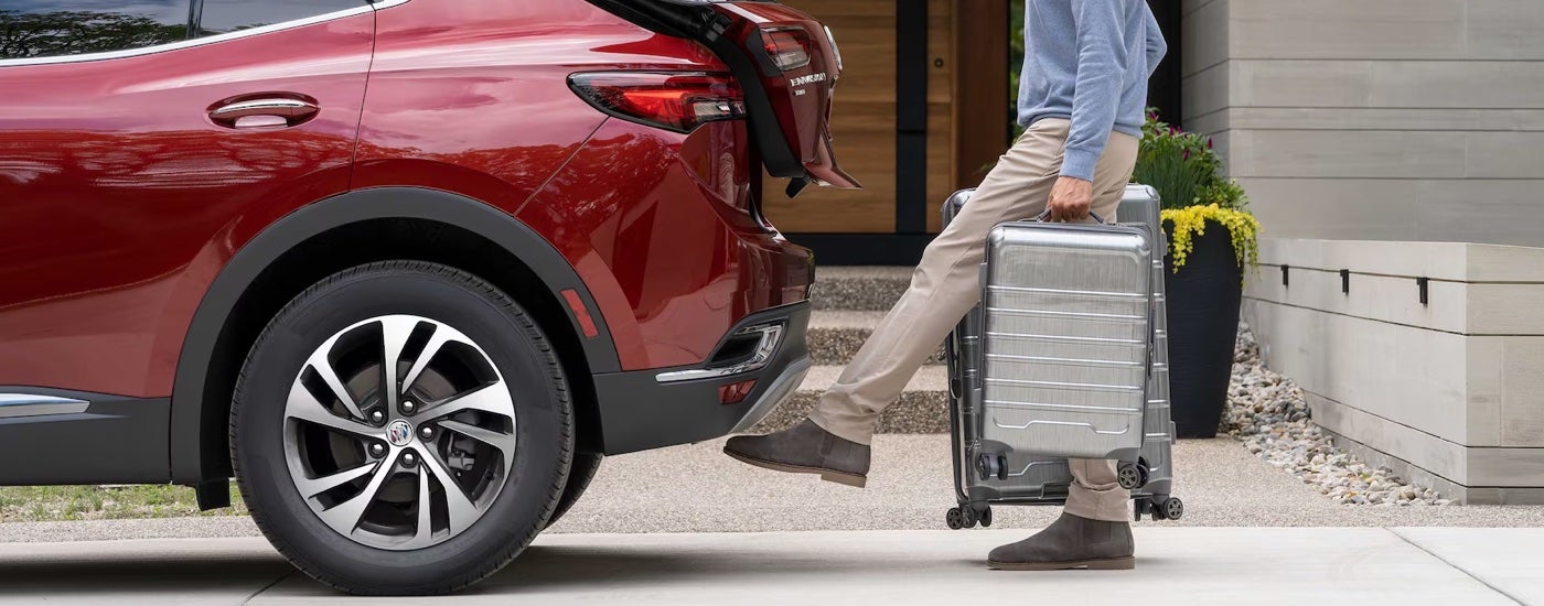 A man carrying luggage using his foot to activate the hands free power liftgate on a red 2023 Buick Envision.