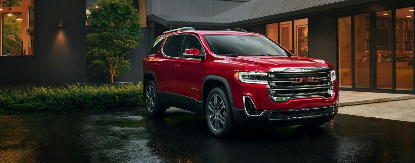 A red 2023 GMC Acadia SLT parked in the driveway of a modern house.